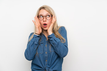 Young blonde woman over isolated white wall with glasses and surprised