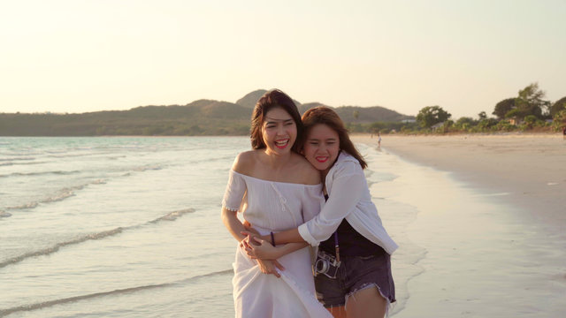 Young Asian Lesbian Couple Running On Beach. Beautiful Women Friends Happy Relax Having Fun On Beach Near Sea When Sunset In Evening. Lifestyle Lesbian Couple Travel On Beach Concept.