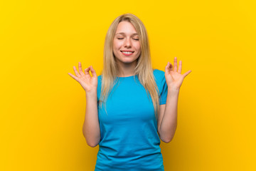 Young blonde woman over isolated yellow background in zen pose