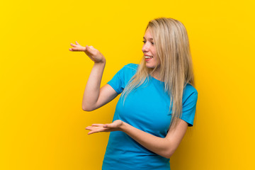 Young blonde woman over isolated yellow background holding copyspace to insert an ad