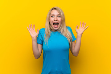 Young blonde woman over isolated yellow background with shocked facial expression