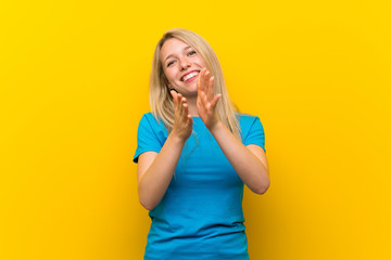 Young blonde woman over isolated yellow background applauding after presentation in a conference