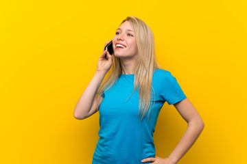 Young blonde woman over isolated yellow background keeping a conversation with the mobile phone