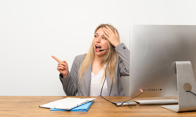 Young woman working with headset surprised and pointing finger to the side