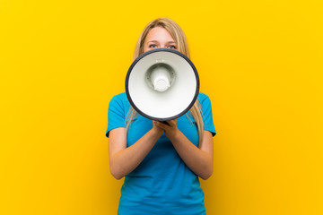 Young blonde woman over isolated yellow background shouting through a megaphone