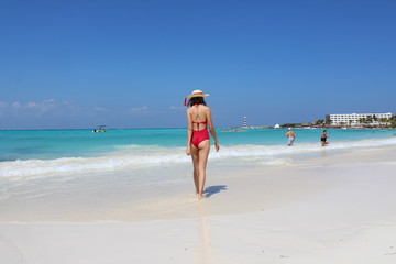 Fototapeta na wymiar Mujer con traje de baño color rojo caminando en las playas de arena blanca de cancun caribe mexicano