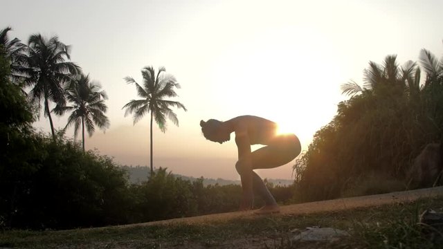 young woman gets into mountain position doing surya namaskar in tropical wood at sunrise side view low angle shot slow motion. Concept fitness yoga wellness lifestyle