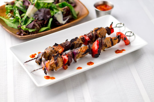 Two pork kebab brochettes in a white plate. These delicious pork meat souvlaki were roasted on the bbq until well-grilled. Cooking food on skewers has been common in many cuisines since ancient times.