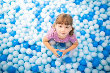 Fototapeta na wymiar Happy little girl child in colourful blue plastic balls pool.
