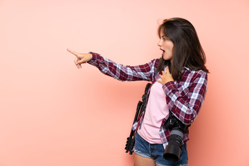 Young photographer girl over isolated pink background pointing finger to the side