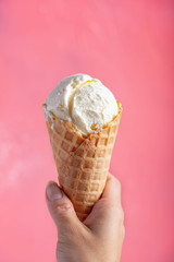 holding vanilla icecream in waffle cone on pink background