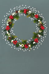Christmas wreath decoration with decorative snowflakes, holly berries, mistletoe, spruce fir, pine cones and silver ball baubles on grey background. Traditional symbol for the festive season.