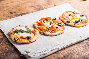 Several ready-made mini pizza, pizzetta on a linen napkin on a wooden table
