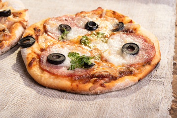 Traditional Italian appetizer - mini pizza, pizzetta with sausage, olives and mozzarella cheese on a linen napkin close-up - Neapolitan style