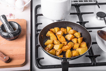 Men's rustic breakfast - fried potatoes with eggs and cherry tomatoes in a pan, standing on the stove