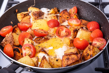 Rustic breakfast for men - fried potatoes with eggs and cherry tomatoes in a pan, close-up, top view
