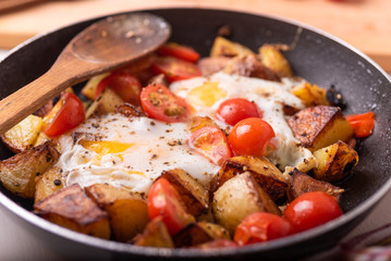 Traditional rural simple dish - fried potatoes with eggs and cherry tomatoes in a pan closeup.