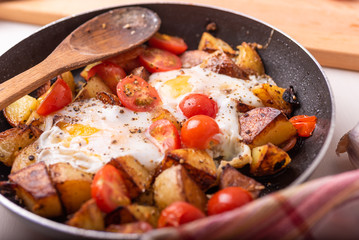 Traditional rural simple dish - fried potatoes with eggs and cherry tomatoes in a pan closeup