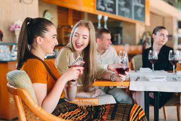 Friends have fun drinking wine, talking and smiling in the restaurant.