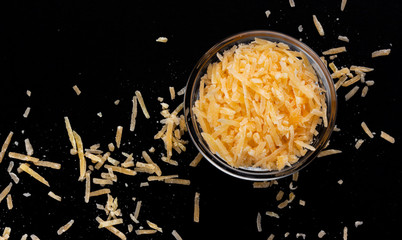 Grated parmesan cheese on black background, top view