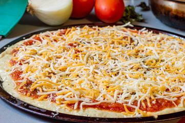 Raw uncooked homemade pizza and ingredients on grey worktop