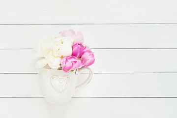 White mug with heart for hot drink with a peonies  inside, on white background. Copy space. top view.