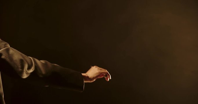 Close up shot of hand of unrecognizable orchesra conductor waving his stick and directing musicians during a rehearsal. Studio shot on black background 4k footage