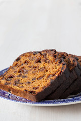 Fruit loaf cake sliced on a decorated blue and white plate.  On a white wood background