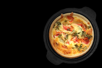 Tomato and spring onion quiche in a cast iron pot dish.  On a black background