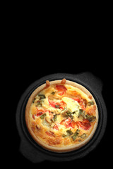Tomato and spring onion quiche in a cast iron pot dish.  On a black background