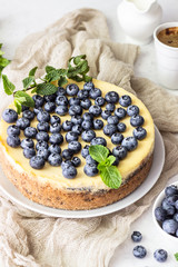 New York style cheesecake, fresh blueberries and mint on a white plate. Light stone background. Copy space.