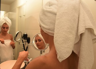young woman in a white towel on her head holding a toothbrush with paste in a bathroom room in...