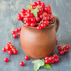 Ripe red berries of a currant in a brown clay mug on an old wooden table. Selective focus.