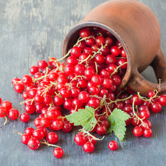 Ripe red berries of a currant in a brown clay mug on an old wooden table. Selective focus.