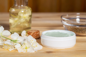 Jar of cream made from natural plant ingredients, oils and herbs, jasmine flowers on a light wooden background - preparation of organic cosmetics concept