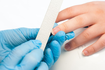 Closeup shot of a woman in a nail salon receiving a manicure by a beautician with nail file. Woman getting nail manicure. Beautician file nails to a customer.