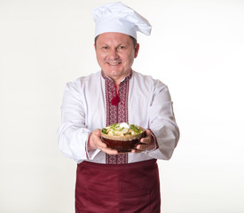 Chef keeps tasty dumplings in his hands. Cook man in slavic national clothes: cap, apron and embroidered.