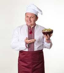 Chef keeps tasty dumplings in his hands. Cook man in slavic national clothes: cap, apron and embroidered.