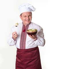 Chef keeps tasty dumplings in his hands. Cook man in slavic national clothes: cap, apron and embroidered.