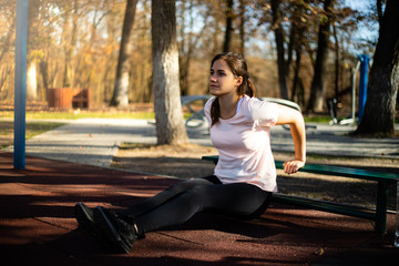 Beautiful woman doing sport on outdoor park during fall and sunset - triceps exercise