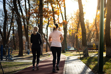 Obraz premium Two beautiful fit women running in parks during fall and suns
