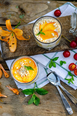 Two galasses of peach panna cotta with white and orange layers. Served outdoor on wooden background...