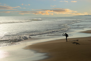 Lone surfer exercising on empty beach at sunset, casting shadow on the sand