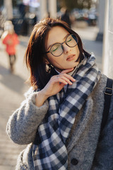 Attractive young girl wearing glasses in a coat walking on a sunny day