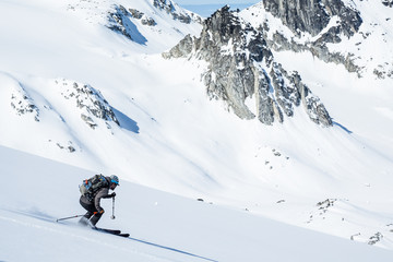 Skier sliding down steep slope overlooking the Snowbird Glacier in the Talkeetna Mountains of Alaska.