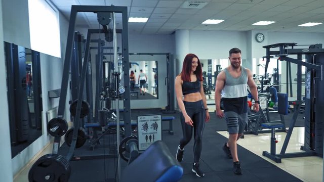 Muscular man and attractive woman in sports club. Modern background of fitness center and a happy couple coming to do their workout.