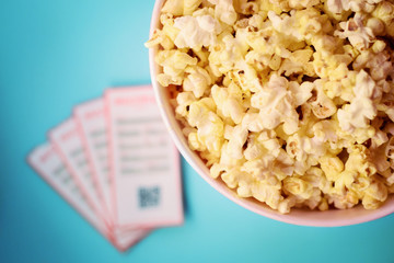 Top view of box with popcorn and 4 tickets for movie laying near on blue table