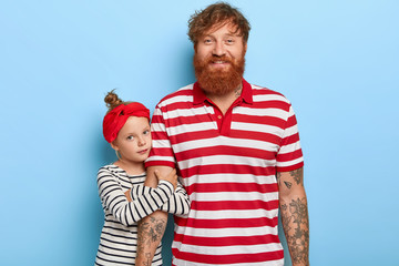 Lovely girl wears red headband, striped sweater embraces hand of father, expresses love and care,...