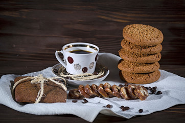 Sweet dessert with coffee, a stack of oatmeal cookies and gingerbread on a white linen tablecloth, wooden background, mood