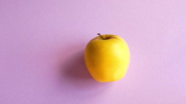 The yellow apple is rolling on the purple table and stay